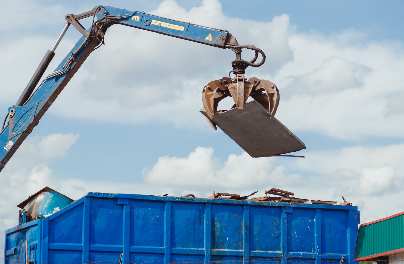 Crane dropping scrap metal into a commercial dumpster. 