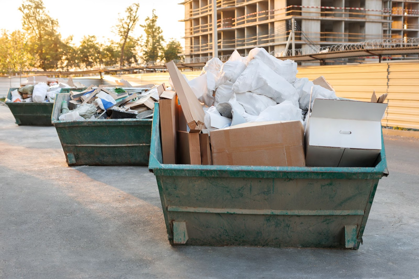 Three dumpsters overflowing with construction debris next to an active job site.