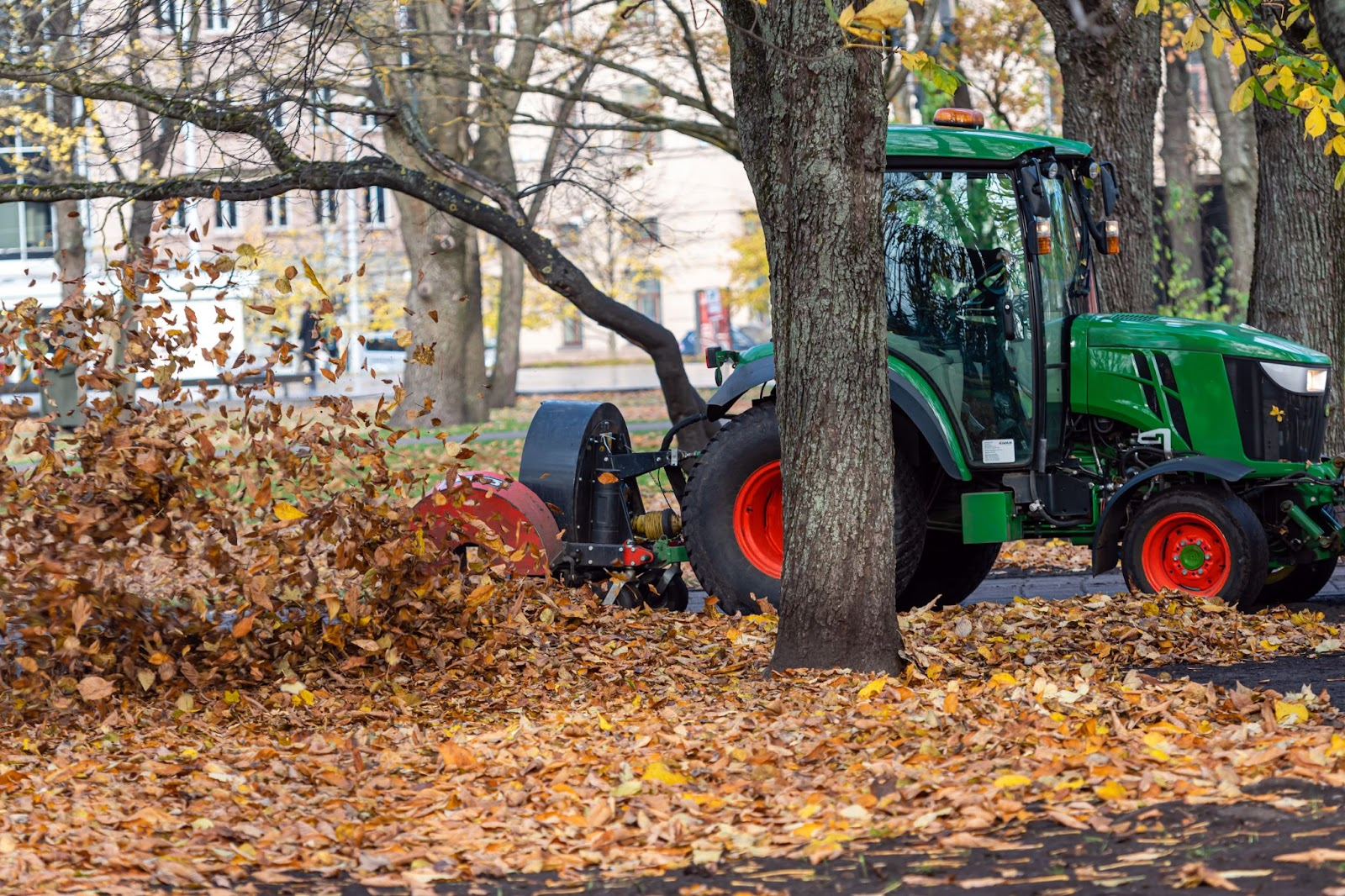 Tractor with a blower clearing grass clippings and debris from a city park lawn 
